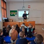Nauczyciel prowadzi zajęcia edukacyjne w klasie, w tle tablica z napisem WIOSNA, na podłodze na materacach siedzą zainteresowani uczniowie
