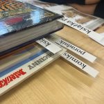 Biurko z książkami, stronami komiksów i magazynem. Paski papieru z tekstem „Kasia” i „Poradnik” wystają ze stosu. Nieopodal spoczywają ręce. W rogu znajduje się emblemat RODLA SP7.