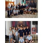 Dwie grupy uczniów w niebieskich mundurkach pozują do zdjęć na tle historycznych transparentów i portretów na szkolnym korytarzu.