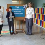 Dwóch chłopców i dwie kobiety stoją na korytarzu szkolnym podczas ceremonii wręczenia nagród w konkursie ortograficznym.