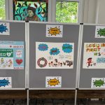 Trzy plakaty projektów uczniowskich na szarych tablicach, każdy z kolorowymi rysunkami i polskim tekstem, wyeksponowane w pomieszczeniu.