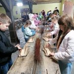 Dzieci pracują przy długim stole w warsztacie, używając patyków i desek.