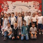 Grupa małych dzieci pozuje razem na tle kolorowej sceny teatralnej w Poznaniu.