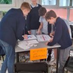 Czterech uczniów pracuje razem przy stole nad projektem Historia Unii Europejskiej w klasie.