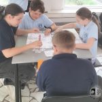 Czworo dzieci siedzi przy stole, pracując nad grupowym ćwiczeniem z planszami i kartami w klasie.