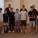 Grupa uczniów i dorosłych stojących w pomieszczeniu; jeden trzyma trofeum, inny znak z napisem 2000.