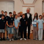 Grupa uczniów i dorosłych pozuje w pomieszczeniu, niektórzy trzymają nagrodę i tabliczkę z napisem 2000.