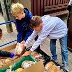 Dwóch chłopców sortuje i rozdaje bochenki chleba na zewnątrz, umieszczając je w skrzynkach i kartonach.