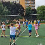 Grupa dzieci grających w siatkówkę na boisku zewnętrznym w pobliżu budynków mieszkalnych.