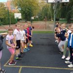 Grupa uśmiechniętych dzieci stoi w dwóch rzędach na boisku sportowym, gotowa do zajęć.