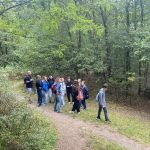 Grupa ludzi stoi na leśnej ścieżce otoczonej drzewami i zielenią.