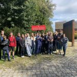 Grupa nastolatków pozujących na zewnątrz przy czerwonym znaku z napisem Rezerwat Przyrody Meteoryt Morasko.