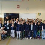 Grupa młodych uczniów i nauczyciel pozują razem w klasie, uśmiechając się do kamery.