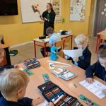 Nauczyciel czyta książkę młodym uczniom, którzy rysują i piszą przy swoich biurkach w klasie.