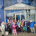 Grupa dzieci w zimowych strojach stoi przed wejściem na stadion Lecha Poznań.