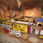 Pokój o tematyce egipskiej z malowidłami ściennymi, zdobionym sarkofagiem i historycznymi artefaktami na wystawie.