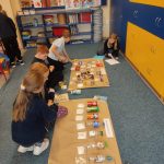 Dzieci w klasie sprawdzają i porządkują różne opakowania i butelki z żywnością na dużych arkuszach papieru na podłodze.