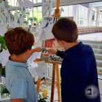 Dwóch chłopców wskazuje na tablicę z papierami i notatkami w jasnym pomieszczeniu.