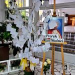 Ekspozycja z drzewem odręcznych notatek i plakatem Prorok Nadziei obok białych róż.