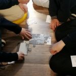 Czworo dzieci siedzi na podłodze i wspólnie układa elementy czarno-białej układanki.