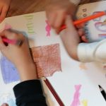 Dzieci kolorujące plakat kredkami i ołówkami, rysujące kształty i kolorowe litery na białym papierze.