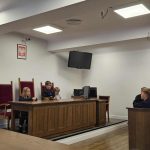 Troje dzieci siedzi na ławce sędziowskiej w sali sądowej, a inne dziecko siedzi przy biurku obok.