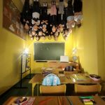 Grupa uczniów stoi do góry nogami na suficie klasy nad ławkami i zieloną tablicą - iluzja