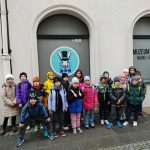 Grupa dzieci pozuje przed Muzeum Iluzji, stojąc przy drzwiach z logo królika.