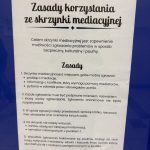 Na ścianie z niebieskim tłem widnieje wydrukowany w języku polskim znak z zasadami korzystania ze skrzynki mediacyjnej.