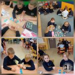 Dzieci w klasie pracują razem nad zajęciami edukacyjnymi w małych grupach przy biurkach i na podłodze.