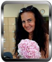 Uśmiechnięta kobieta z długimi ciemnymi włosami trzymająca bukiet różowych hortensji w biurze.