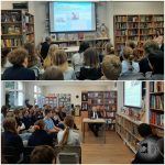 Uczniowie słuchają prezentacji w bibliotece; prezenter siedzi przy biurku z pokazem slajdów na ekranie.