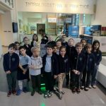 Grupa uczniów pozuje razem w pomieszczeniu pod napisem INTRALOGISTYKA W PRAKTYCE.