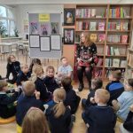 Kobieta czyta grupie małych dzieci siedzących na podłodze w kolorowej bibliotece.