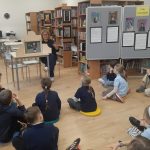 Kobieta czyta grupie dzieci siedzących na podłodze w bibliotece.