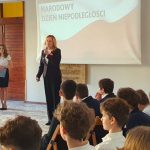 Kobieta przemawia do siedzących uczniów podczas szkolnej uroczystości z okazji Narodowego Dnia Niepodległości.