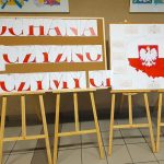 Dwie tablice na sztalugach; na jednej napis "Kochana Ojczyzno Życzymy Ci", na drugiej mapa i herb Polski.