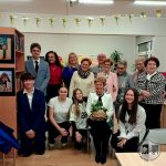 Grupa nastolatków i dorosłych pozujących razem w pomieszczeniu, z jedną kobietą trzymającą kosz z rośliną.