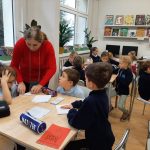 Nauczyciel pomaga młodym uczniom w pracy w klasie wypełnionej książkami i komputerami.