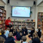 Kobieta czyta grupie dzieci siedzących na podłodze w bibliotece.