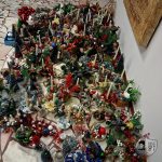 Różnorodne świece bożonarodzeniowe z dekoracjami świątecznymi ułożone na podłodze przy ścianie.