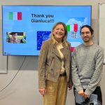 Dwie osoby stoją uśmiechnięte przed ekranem wyświetlającym Thank you Gianluca! i obrazy.