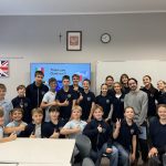 Grupa uczniów i dwoje dorosłych uśmiecha się i pozuje do zdjęcia w klasie.