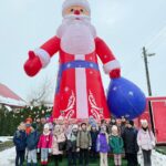 Grupa dzieci pozuje przed dużym nadmuchiwanym Mikołajem na zewnątrz w zimie.
