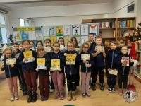 Grupa dzieci stoi w bibliotece, trzymając książki i rysunki Pippi Pończoszanki.