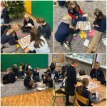 Dzieci siedzą w grupach na podłodze i przy stole, grając w gry planszowe i pisząc na papierze w klasie.