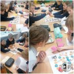 Dzieci w klasie grają razem w edukacyjną grę planszową, siedząc przy biurkach i omawiając karty do gry.