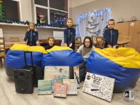 Pięcioro dzieci pozuje z workami fasoli, grami planszowymi i głośnikiem w udekorowanej klasie.