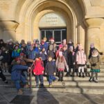 Grupa dzieci w zimowych ubraniach pozuje na kamiennych schodach przed budynkiem centrum kultury.