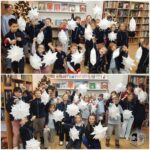 Dzieci w bibliotece trzymające białe papierowe gwiazdki, uśmiechnięte i pozujące do zdjęcia grupowego.